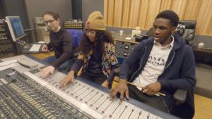 Three people working at an audio mixing board in a recording studio.