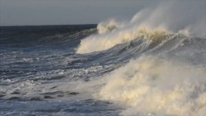 Large ocean waves crashing with white foam under a cloudy sky.