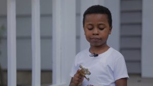 Child in white shirt holding a toy horse, standing outside near white railing.