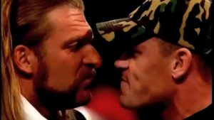 Two men facing each other closely, one with long hair and the other wearing a camouflage cap, in a tense moment.